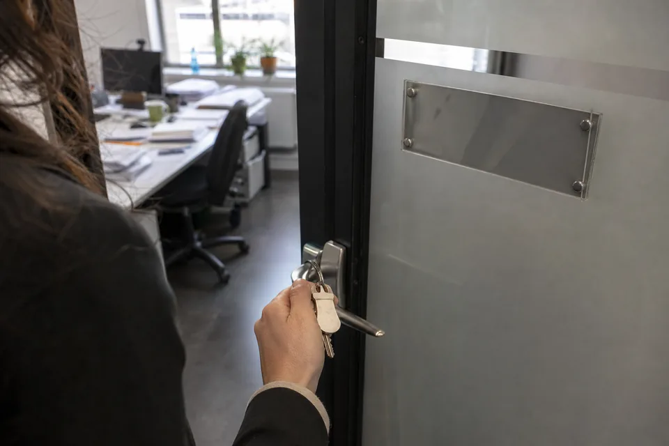 Hand holding a set of office keys in front of a frosted glass door at a small startup office, morning light