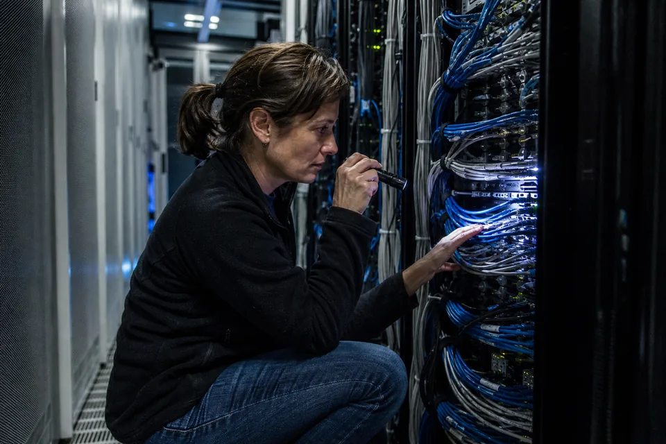 Technician crouching in a colocation data centre aisle reading cable labels on a server rack